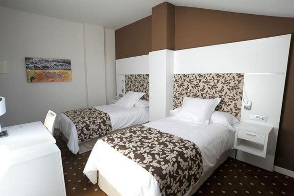 Habitación de hotel con dos camas, cada una con cabecero estampado con motivos florales, ropa de cama blanca y una mesita de noche pequeña con lámpara.