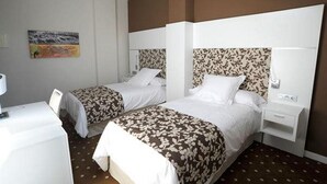 A hotel room with two beds, each with a floral-patterned headboard, white bedding, and a small bedside table with a lamp. - Hotel Alameda Centro (Soria)