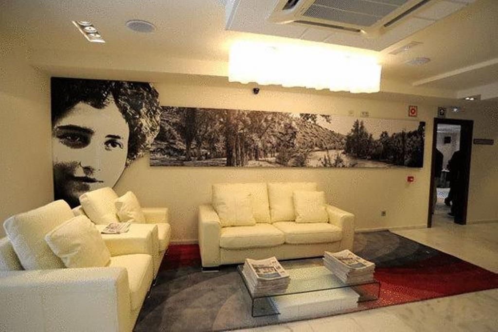 Un vestíbulo moderno con un sofá blanco, una mesa de centro de vidrio con revistas, un cuadro abstracto grande y una alfombra roja.