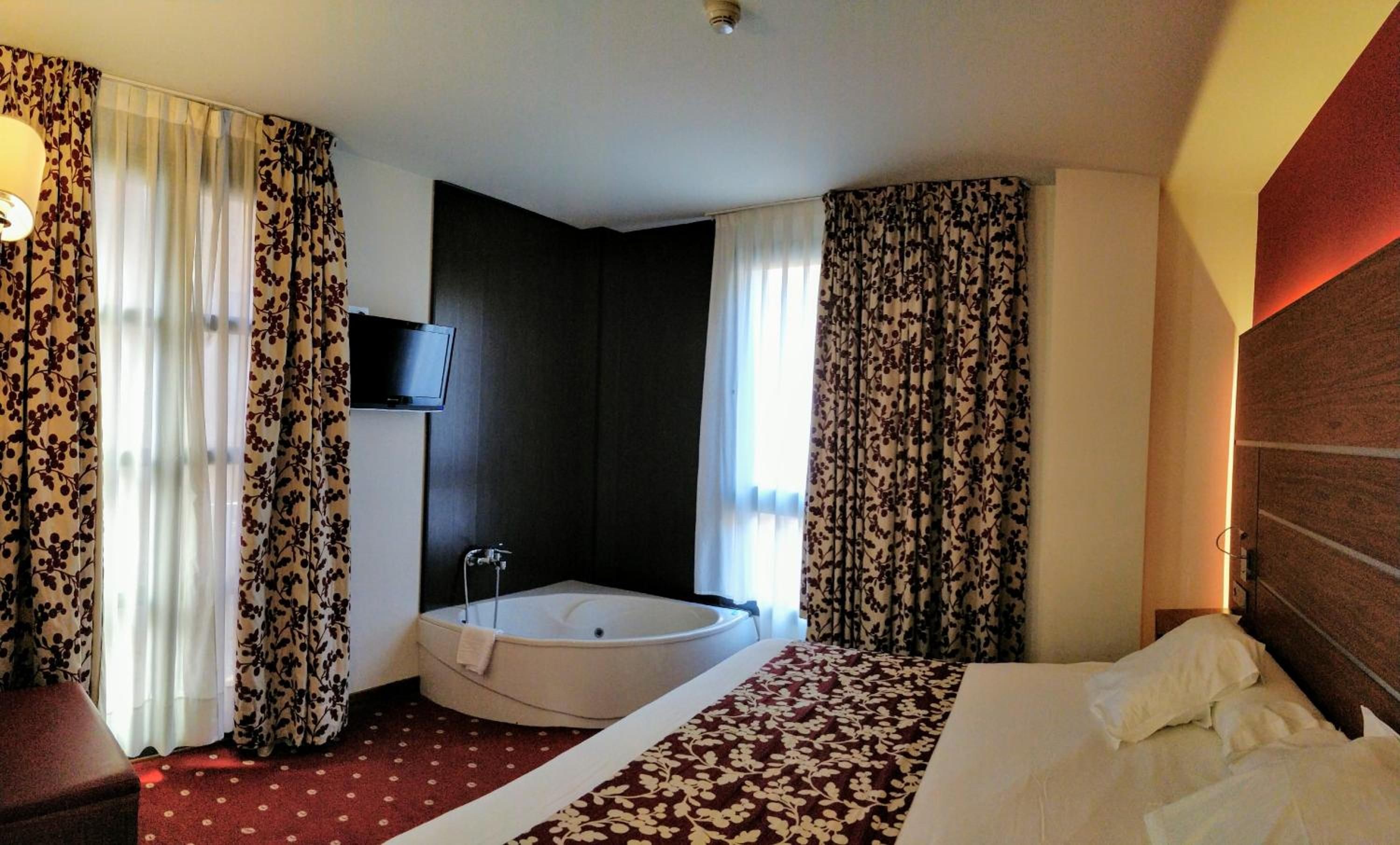 A hotel room with a bed, a bathtub, and curtains.