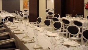 Un salón de banquetes con largas mesas dispuestas para comer, sillas blancas y una paleta de colores neutros.