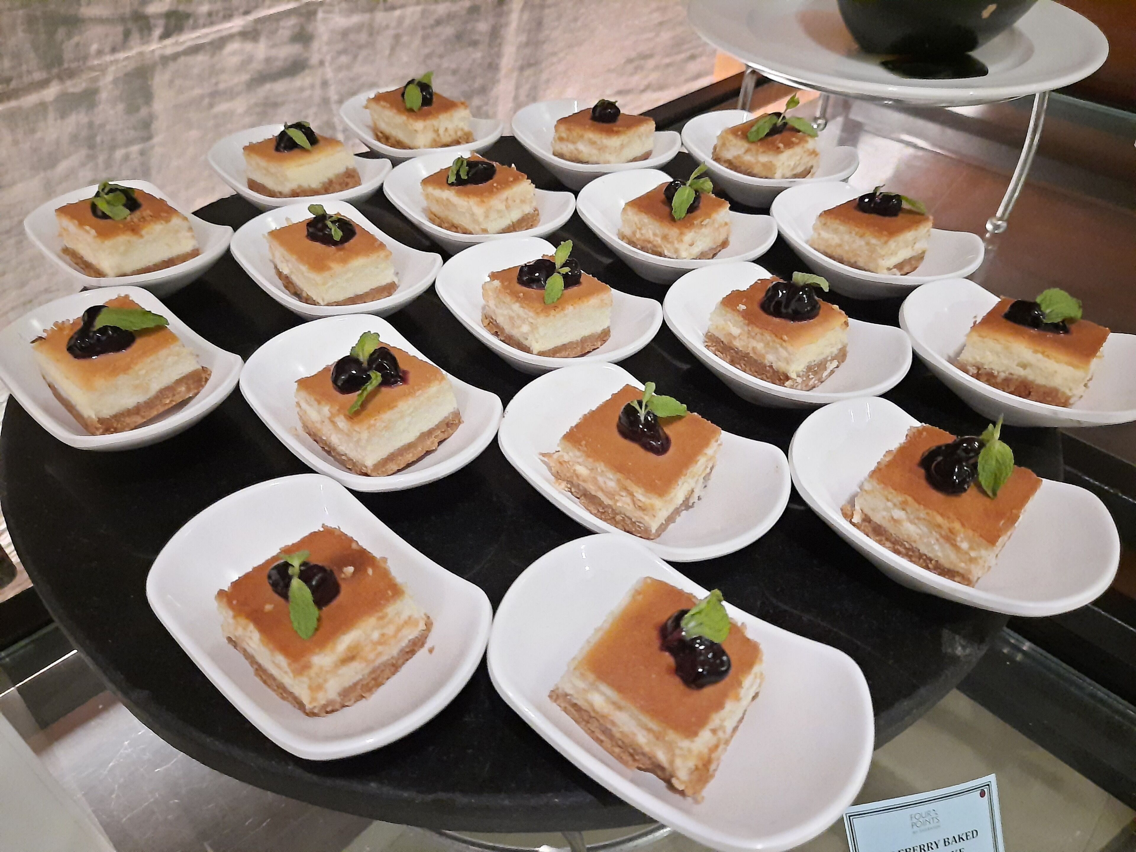 Una presentación de pequeños cuadrados de postre sobre platos blancos, dispuestos en un soporte giratorio.