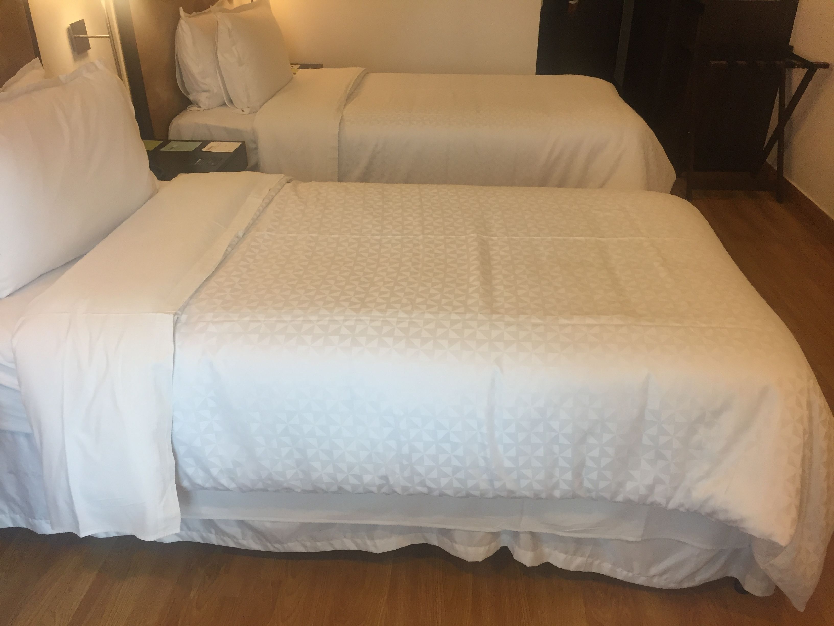 Una cama doble con una colcha estampada, una mesita de noche con lámpara y suelo de madera.
