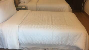 Una cama doble con una colcha estampada, una mesita de noche con lámpara y suelo de madera.