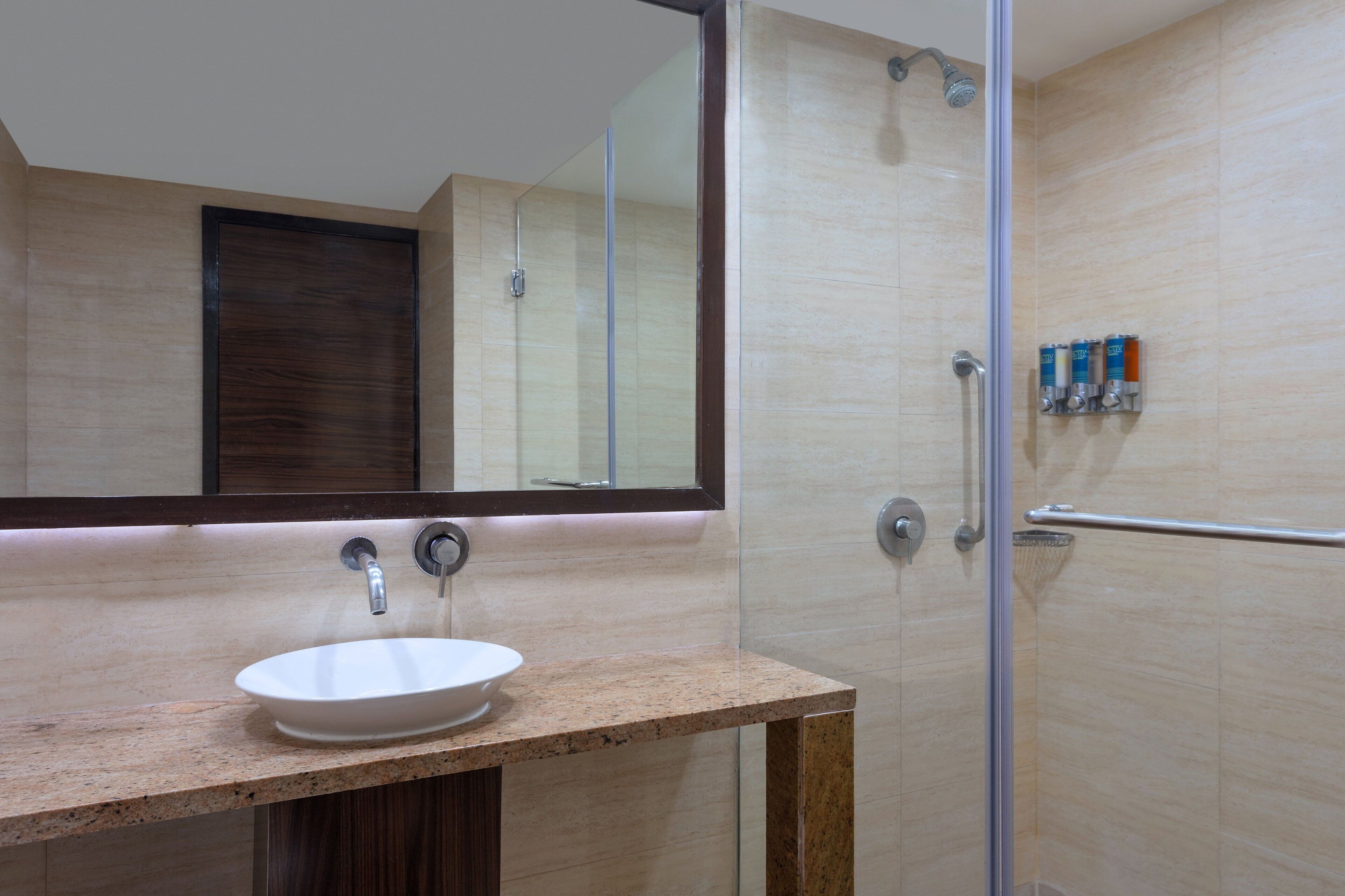 A modern bathroom with a large mirror, a white sink, and a glass shower enclosure.