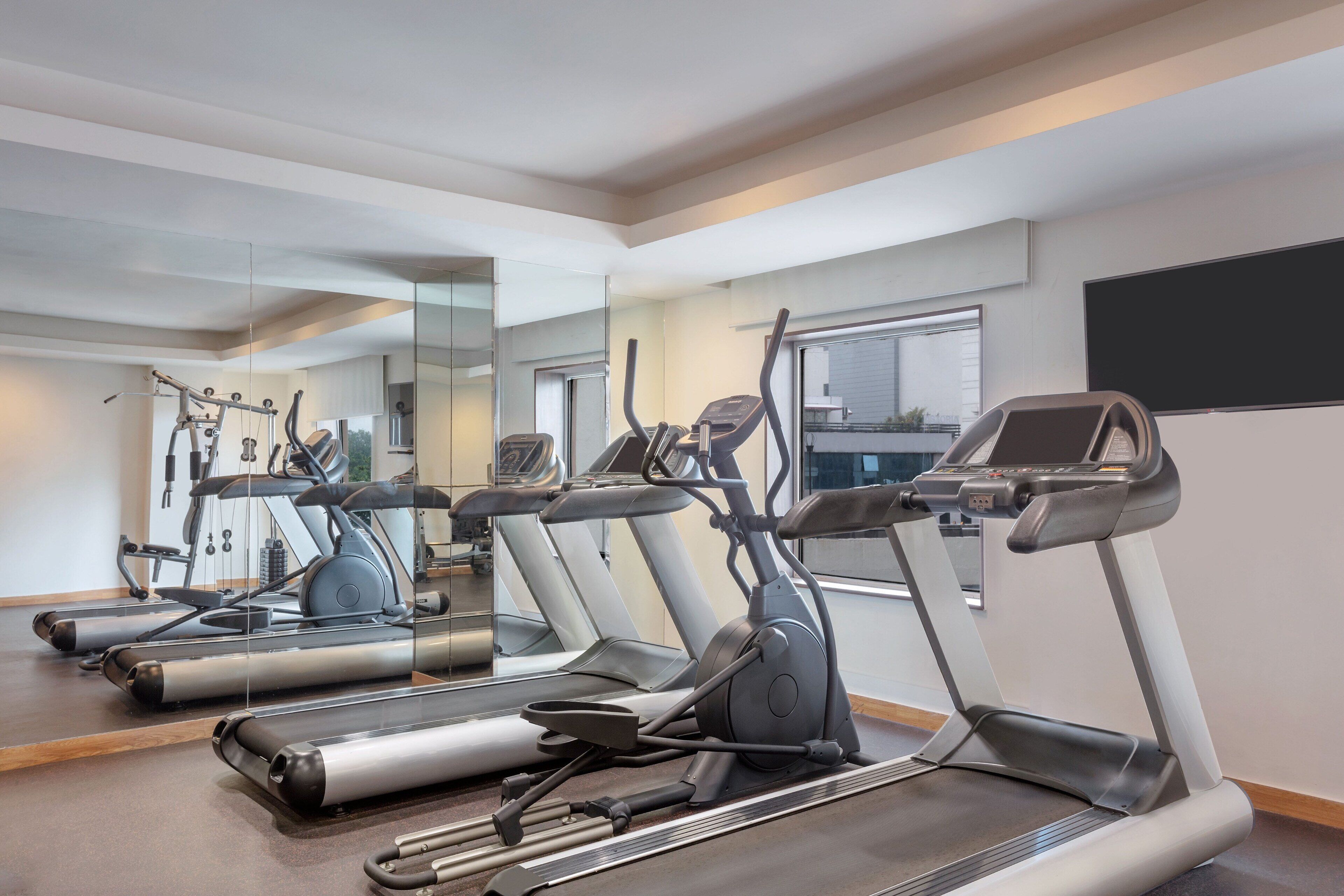 A gym with treadmills, exercise bikes, and a mirrored wall.