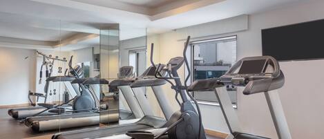 A gym with treadmills, exercise bikes, and a mirrored wall.