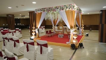 A banquet hall with rows of white chairs with red sashes, a stage with a red carpet, and a floral canopy.