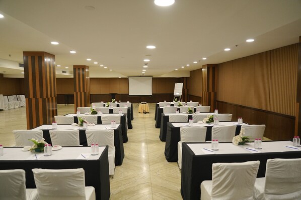 A conference room with rows of tables and chairs, a projector screen, and a podium.
