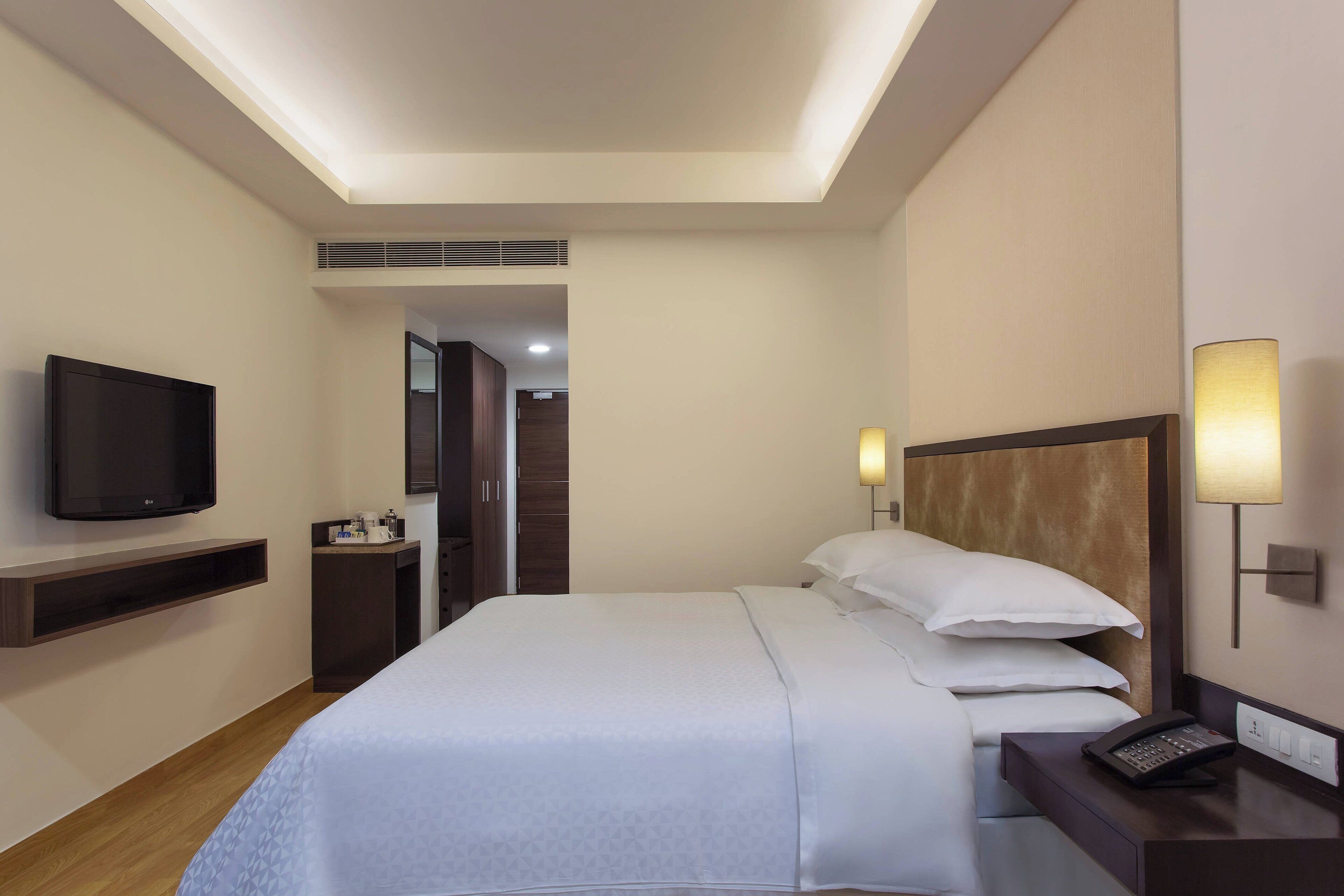 Een hotelkamer met een bed, nachtkastje, lamp, televisie en een klein bureau.