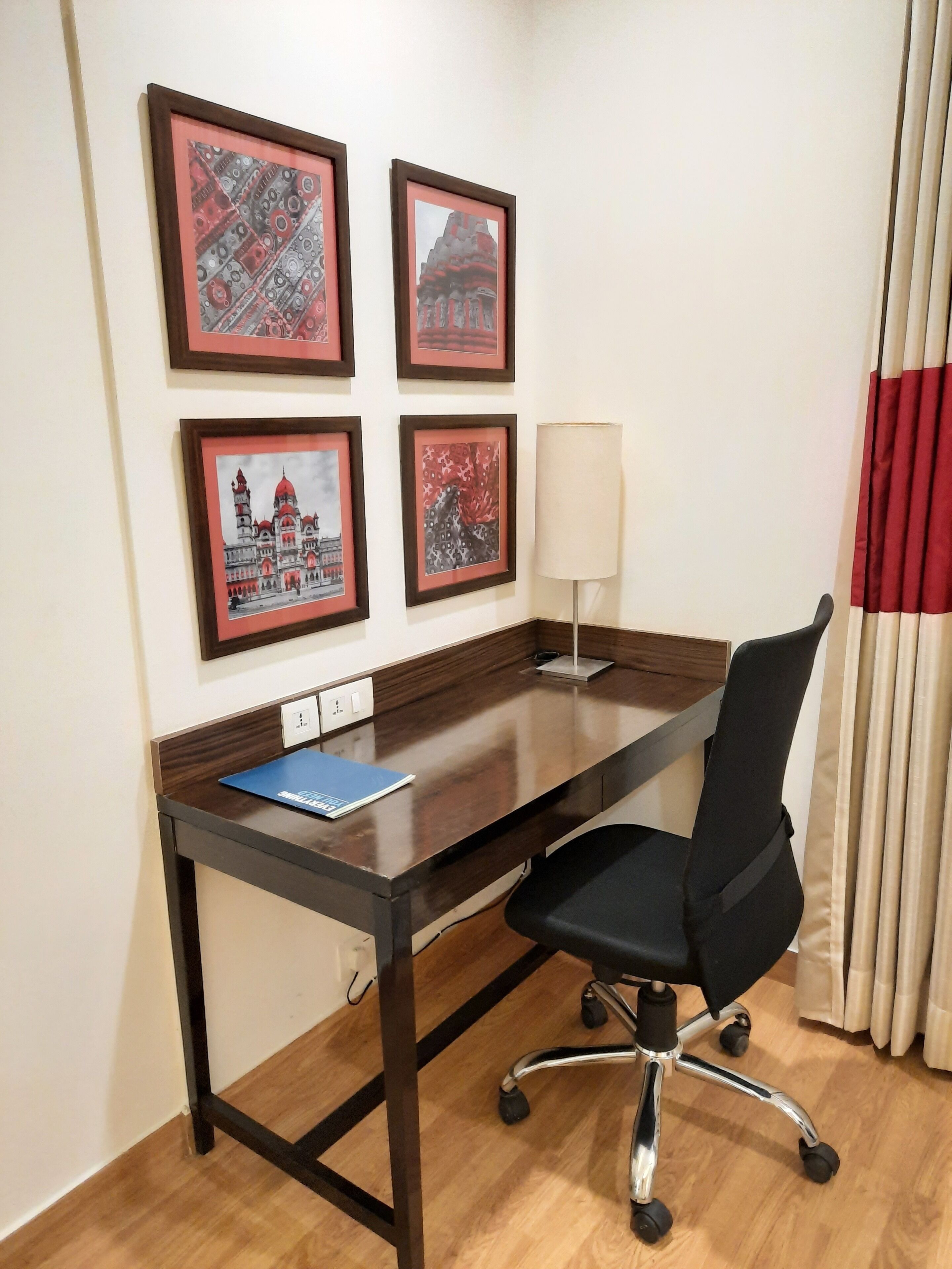 A conference room with a wooden desk, black office chair, and framed artwork on the wall.