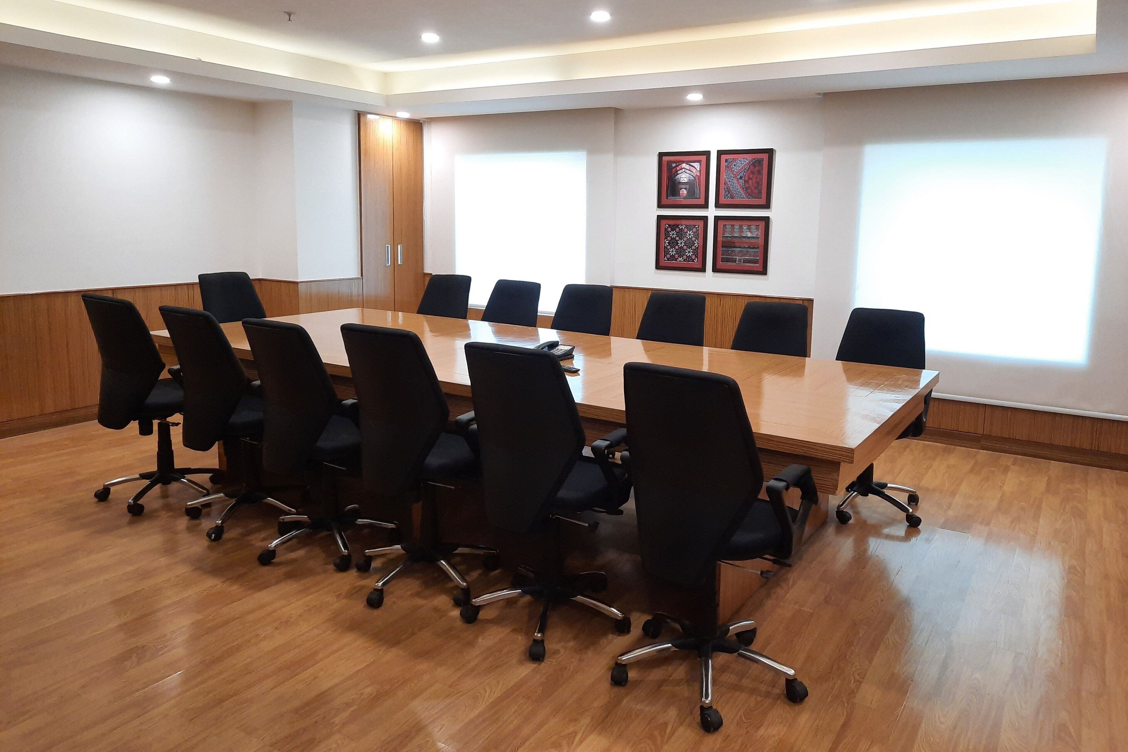 Un salón de conferencias con una larga mesa de madera, sillas de oficina negras y cuadros en la pared.