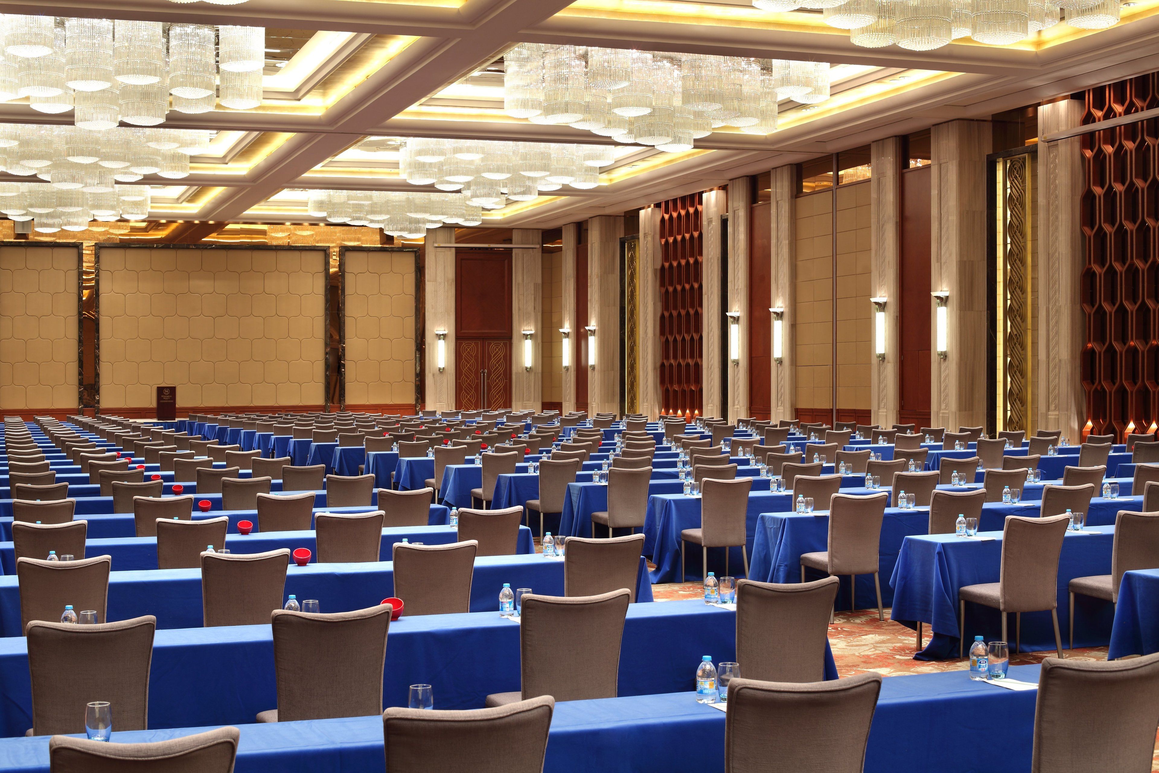 Un amplio salón de conferencias con filas de mesas y sillas, equipado con botellas de agua y tarjetas de identificación.