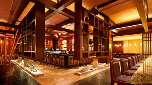 Un restaurante moderno con una barra larga, vigas de madera y suelo de mármol.