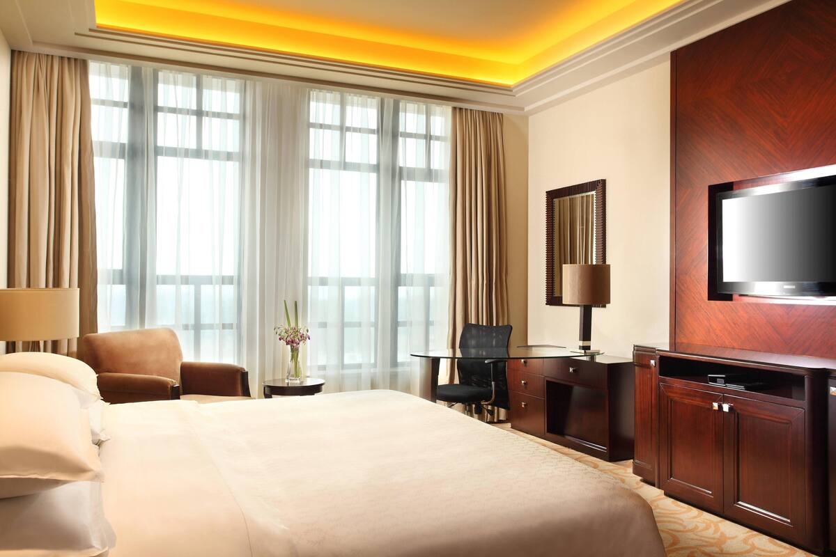 Une chambre d’hôtel avec un grand lit, un bureau avec une chaise, un téléviseur fixé au mur et une fenêtre avec des rideaux.