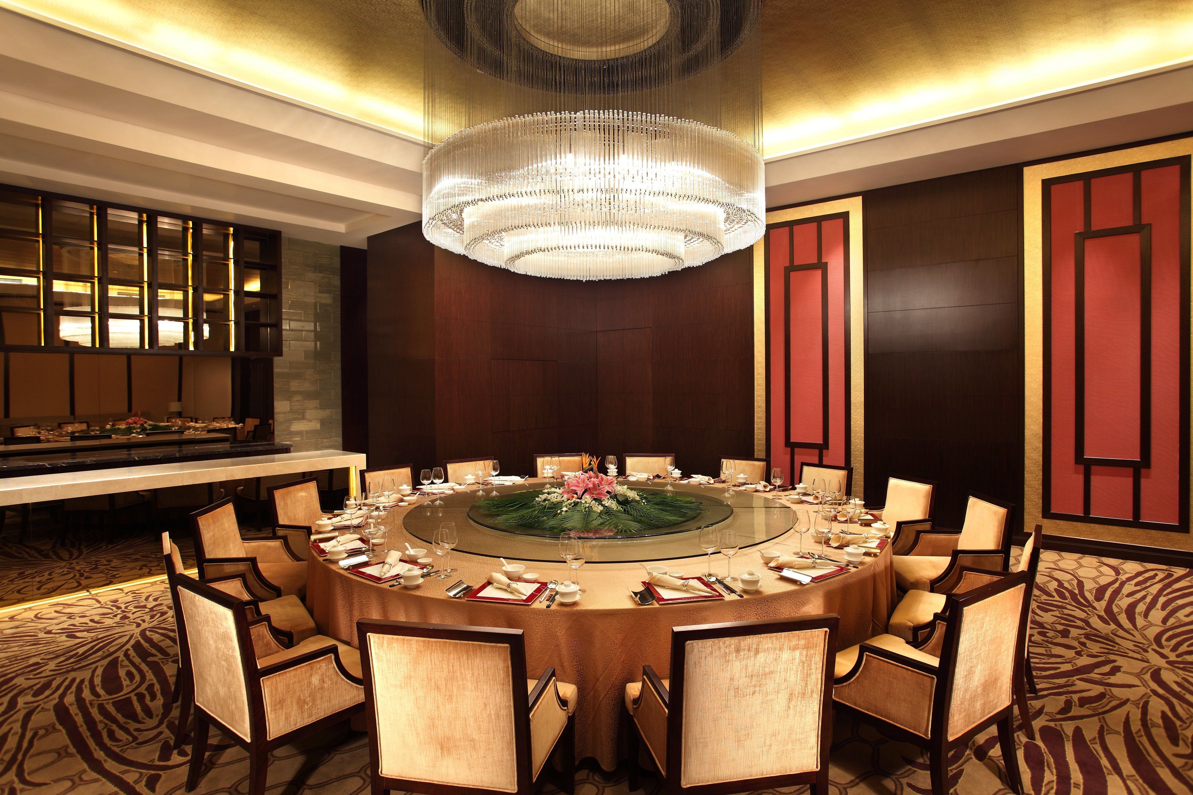 A round table with chairs, a chandelier, and a buffet in a hotel room.