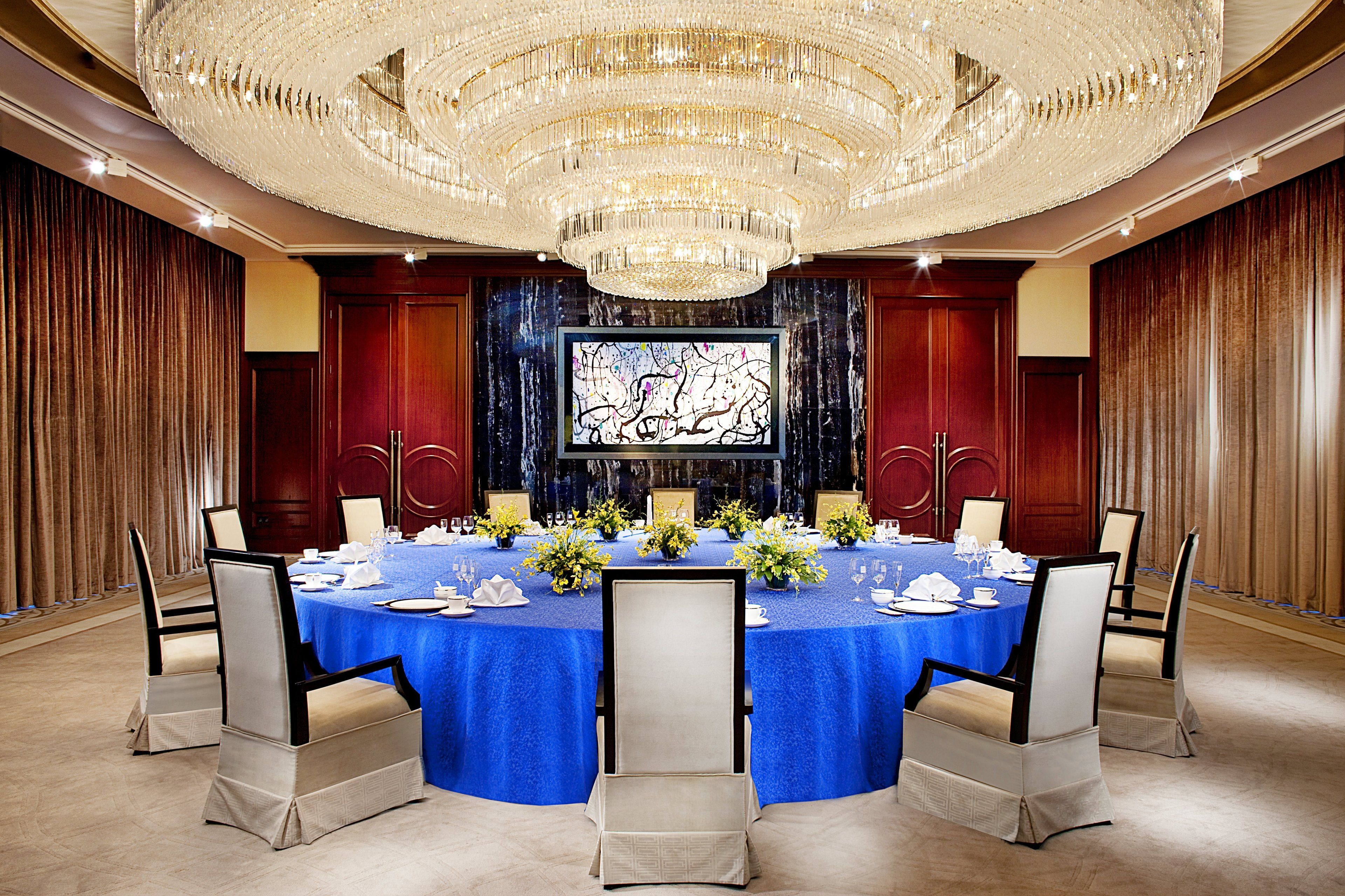 A formal dining room with a round table, blue tablecloth, and white chairs.