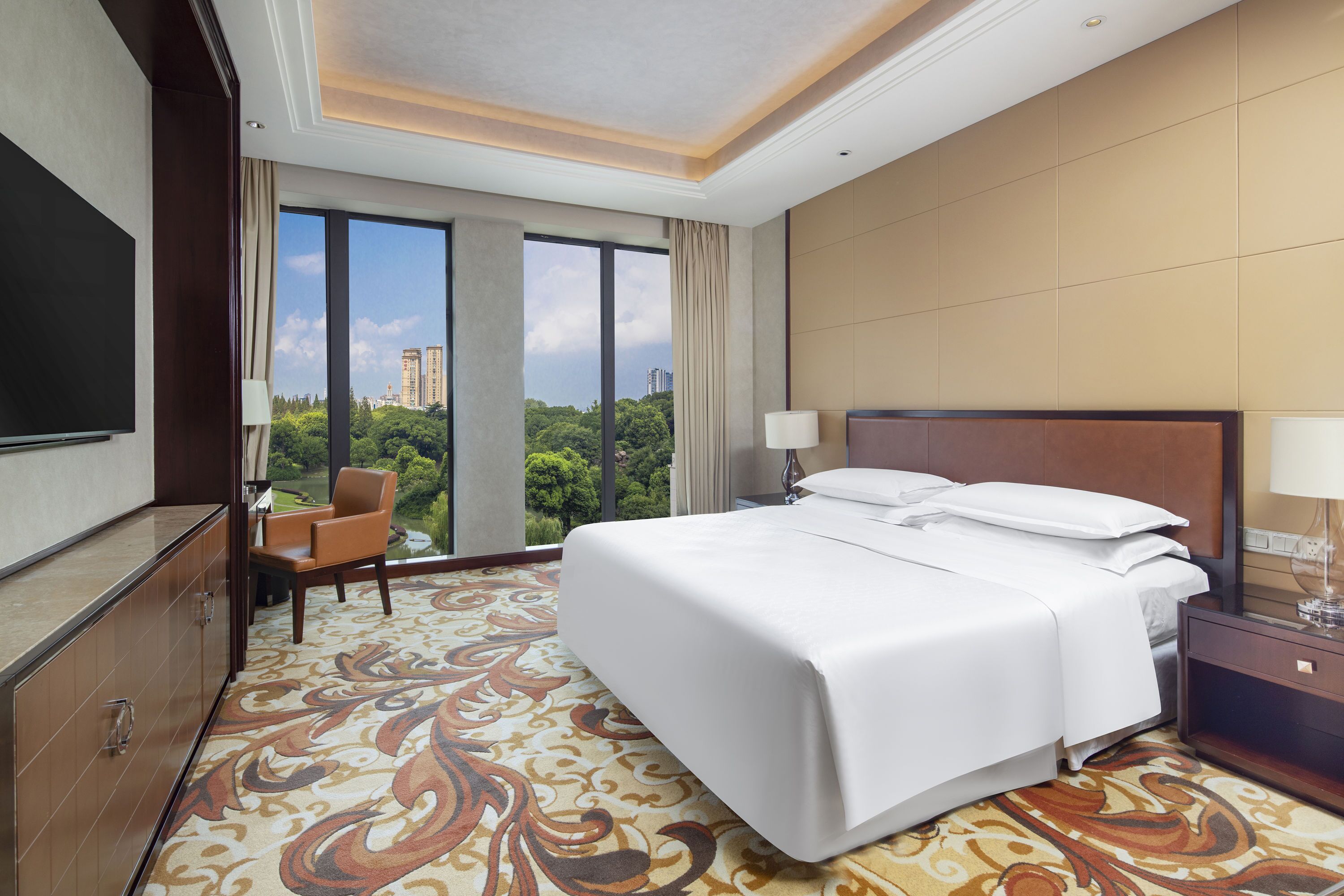Habitación de hotel con una cama grande, televisión, escritorio y vista a la ciudad.