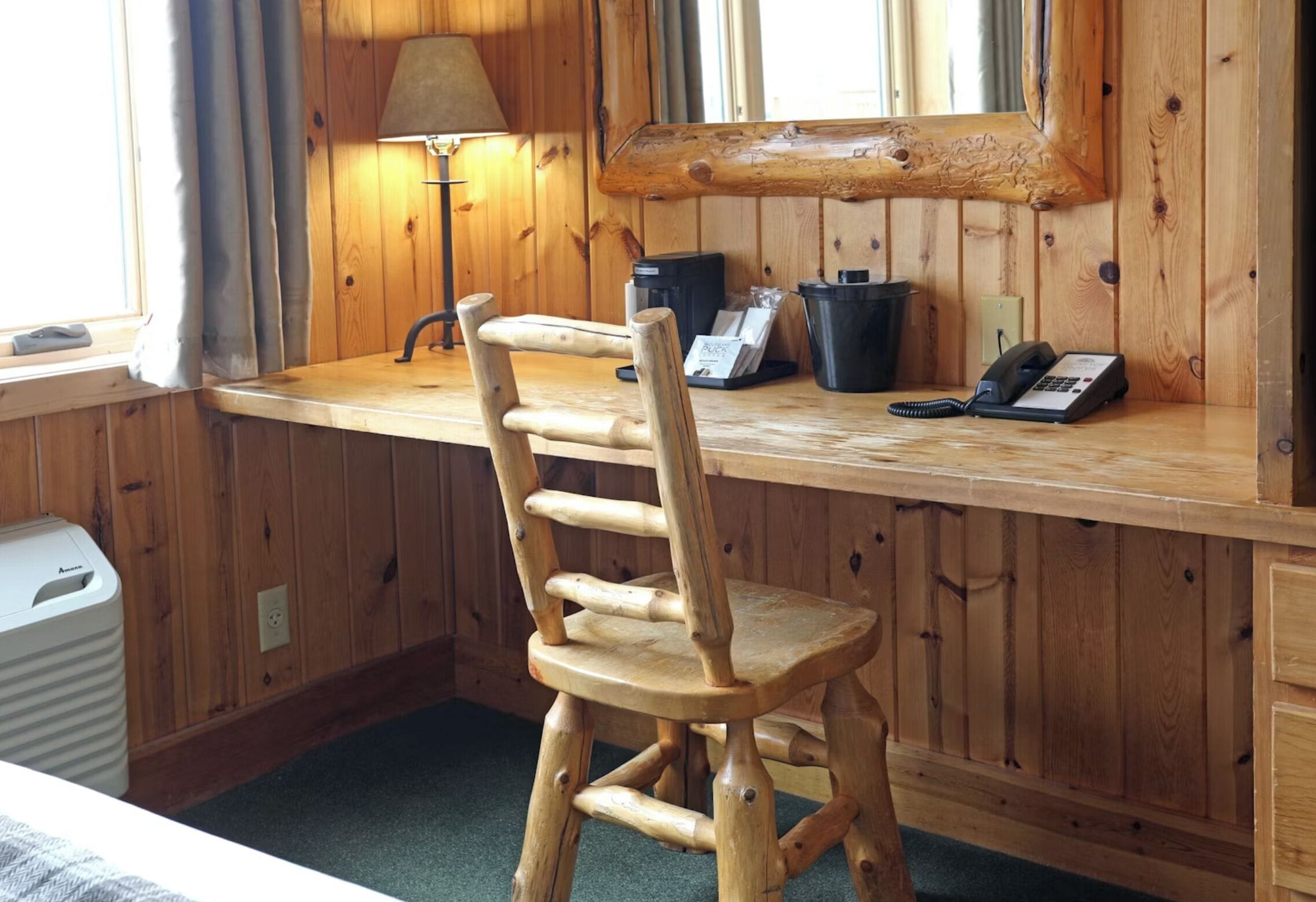 Un bureau en bois avec un téléphone, des poubelles noires et une lampe.