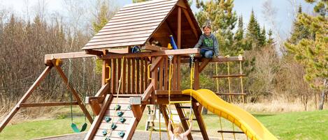 A wooden playground structure with a slide and climbing elements.
