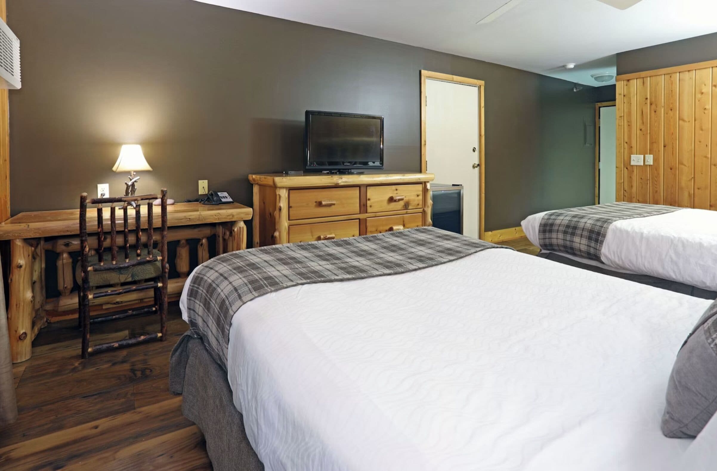 A bedroom with two beds, a desk with a television, a chair, and a lamp.