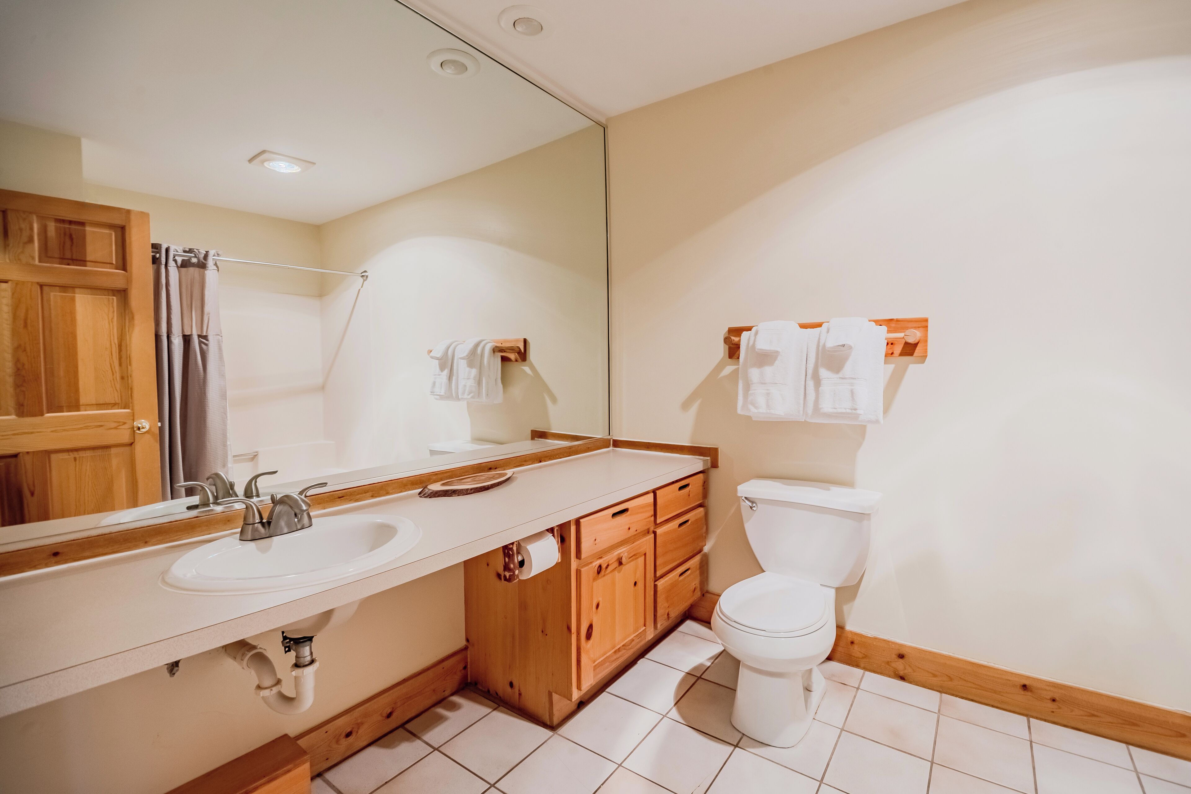 Ein Badezimmer mit Holzwaschtisch, Waschbecken, Spiegel, Toilette und Handtuchhalter.