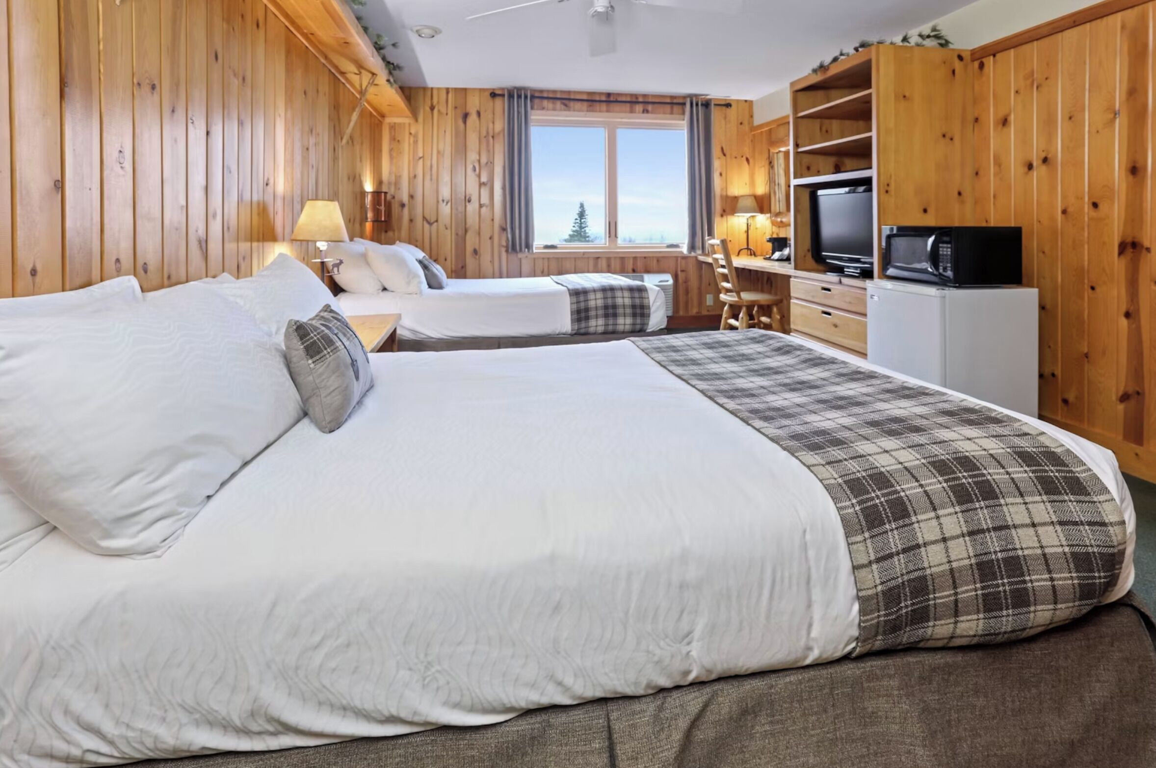 A wooden-paneled room with two beds, a desk, a television, and a microwave.