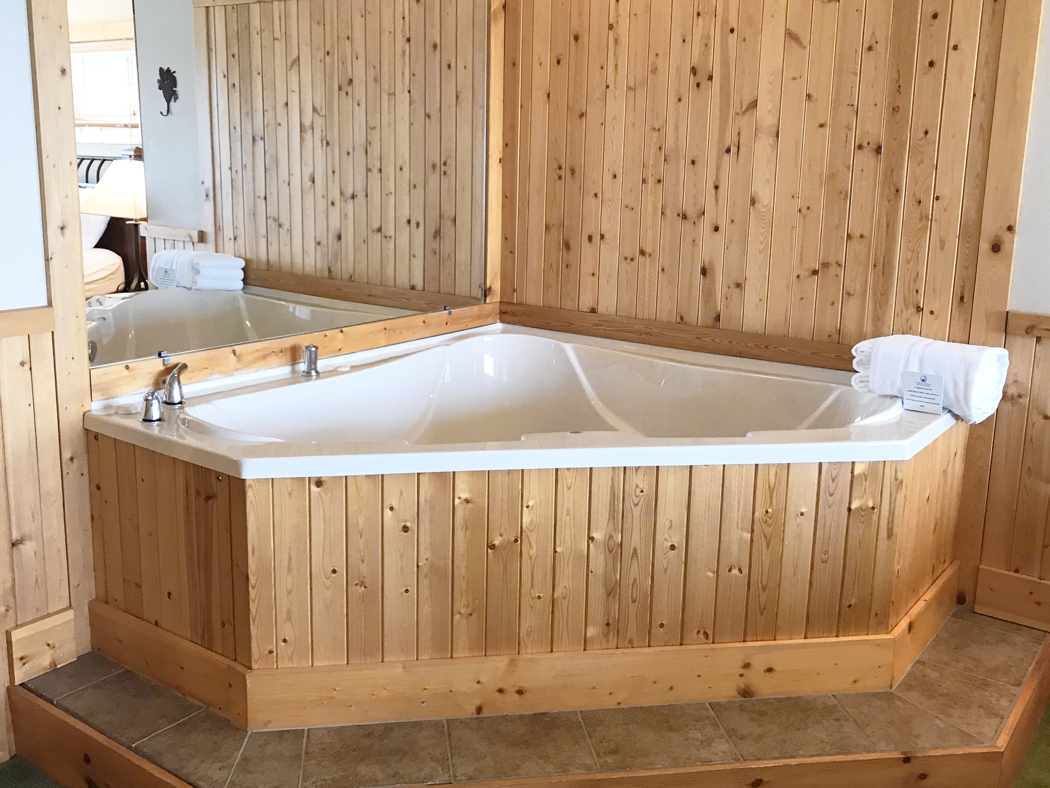 A wooden-paneled room with a large bathtub, a mirror, and a towel on the side.