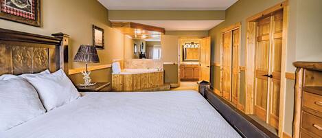 A hotel room with a large bed, wooden wardrobe, a small bathroom with a mirror, and a wooden cabinet.