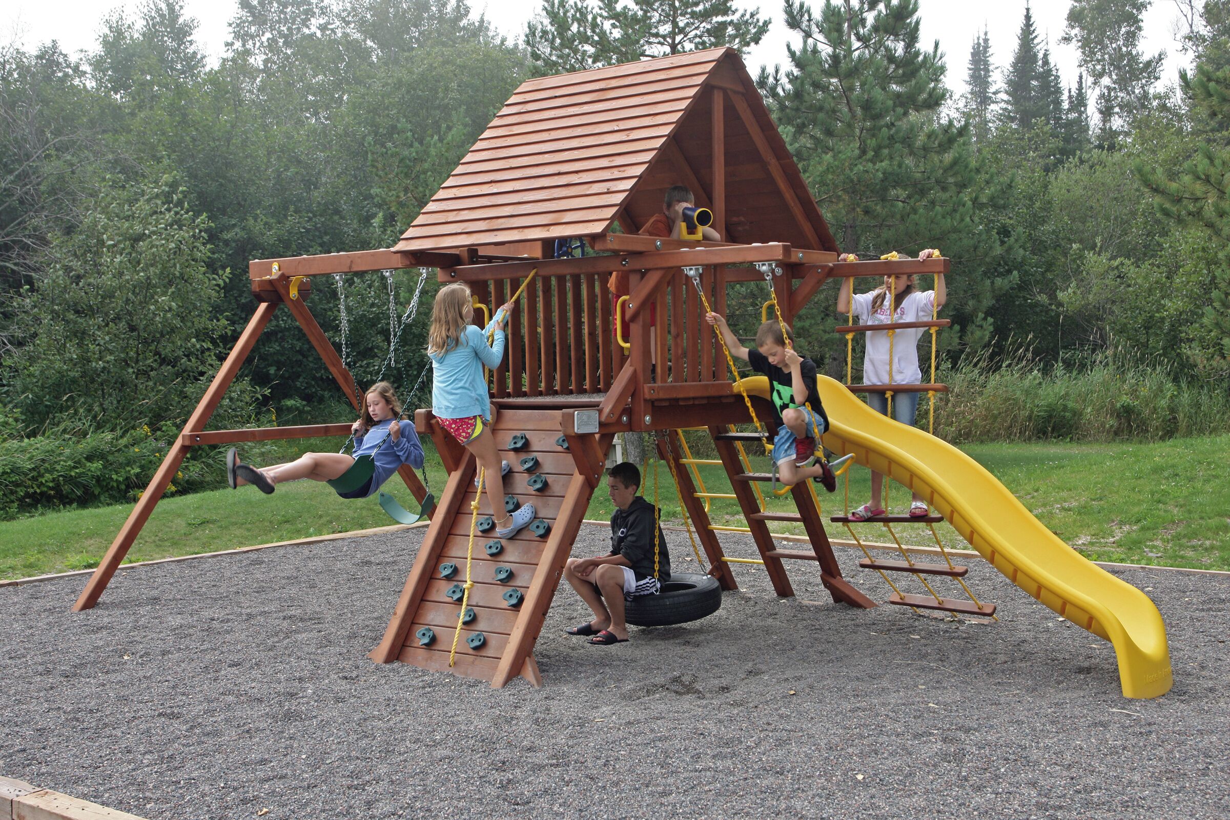 A playground with a wooden climbing structure, a slide, and a tire swing.