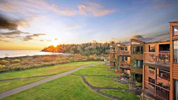 A modern hotel with a view of the sunset over a body of water, surrounded by a well-maintained lawn and a forested area. - Superior Shores  (Two Harbors)
