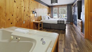 A wooden-paneled room with a large bathtub, a bed with a gray bedspread, and a window with curtains. - Superior Shores  (Two Harbors)