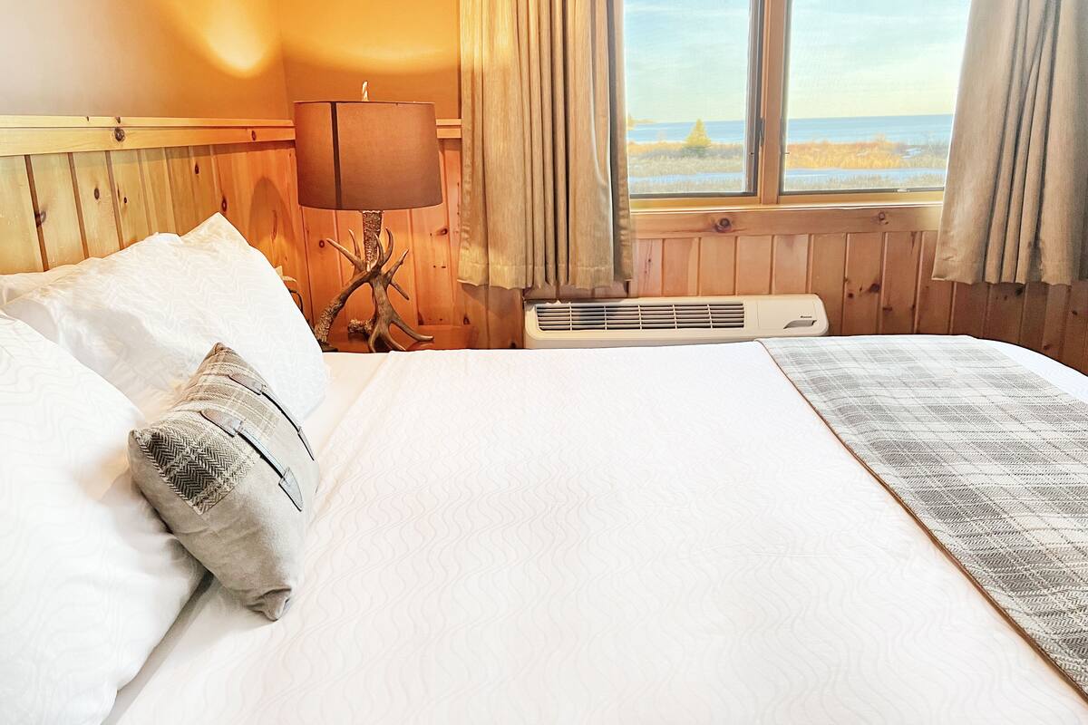 A hotel room with a large bed, a lamp, a heater, and a view of the beach.