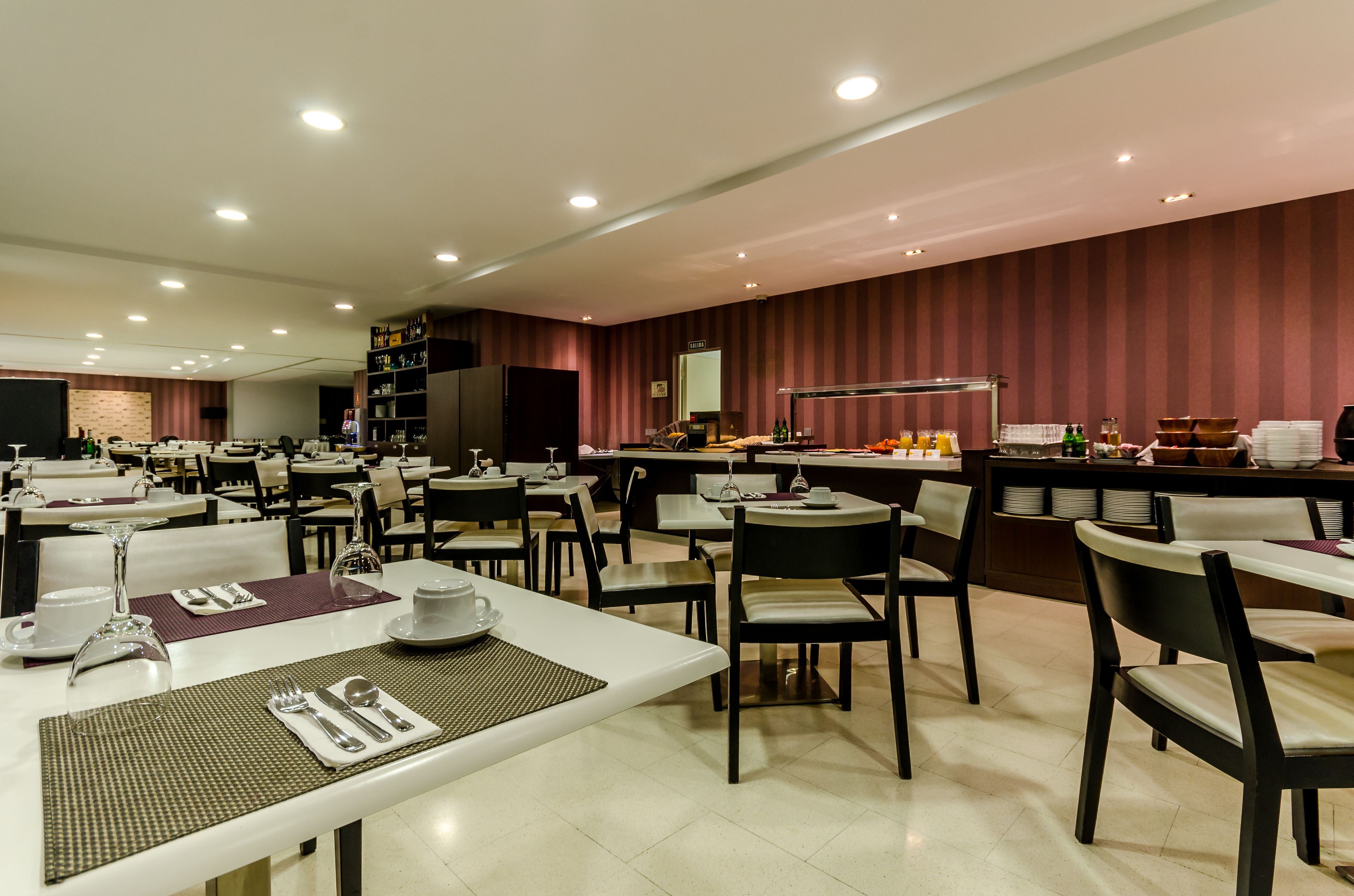 A spacious dining area with multiple tables and chairs, equipped with white table settings and a variety of dining utensils.