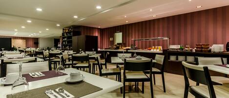 A spacious dining area with multiple tables and chairs, equipped with white table settings and a variety of dining utensils.