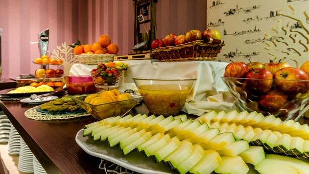 A buffet table with various fruits and vegetables, including apples, oranges, and sliced cucumbers.