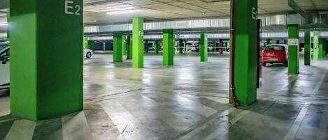 Un parking à plusieurs niveaux avec des piliers verts portant les inscriptions E2 et F2, et une voiture rouge garée au loin.