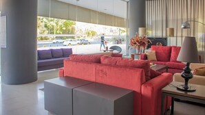 A modern hotel lobby with a red sofa, a grey sectional, and a table with a lamp.