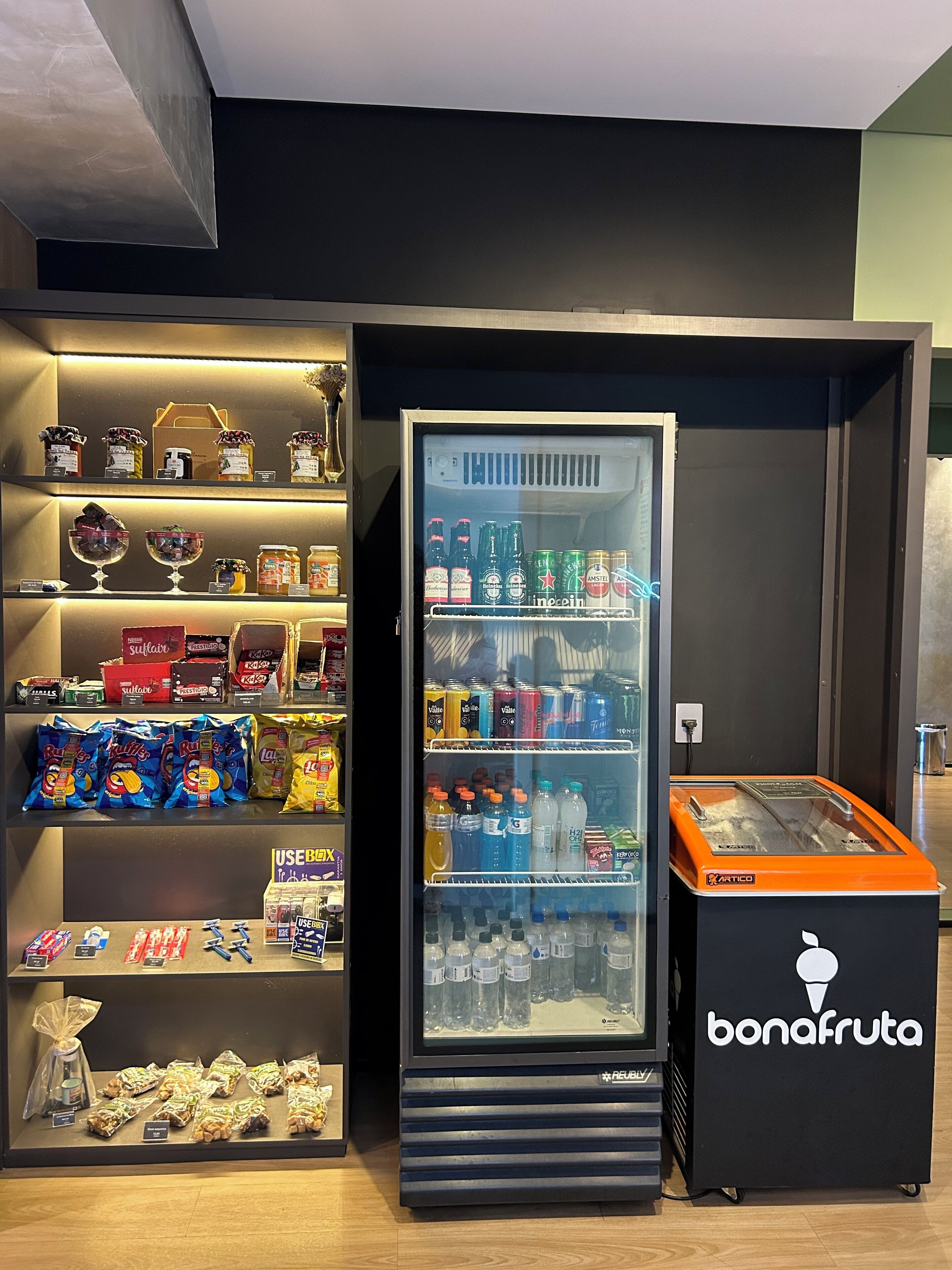 A refrigerated display case with various beverages and snacks, a vending machine, and shelves with packaged goods.