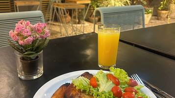 Comida con carne a la parrilla, puré de papas y ensalada sobre una mesa en un espacio exterior con sillas y plantas.