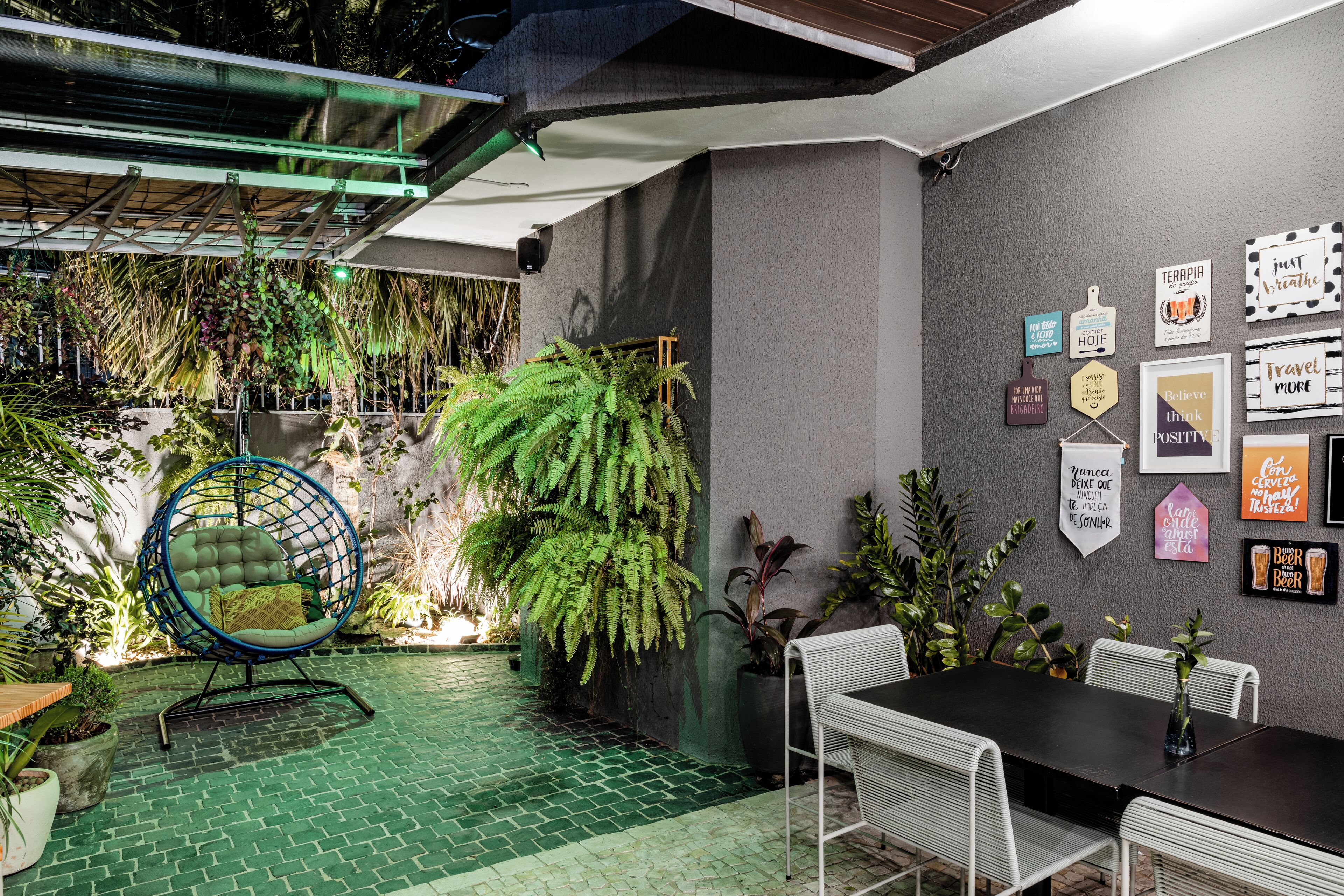 Um jardim interno aconchegante com uma cadeira suspensa, uma mesa de jantar e diversas plantas.