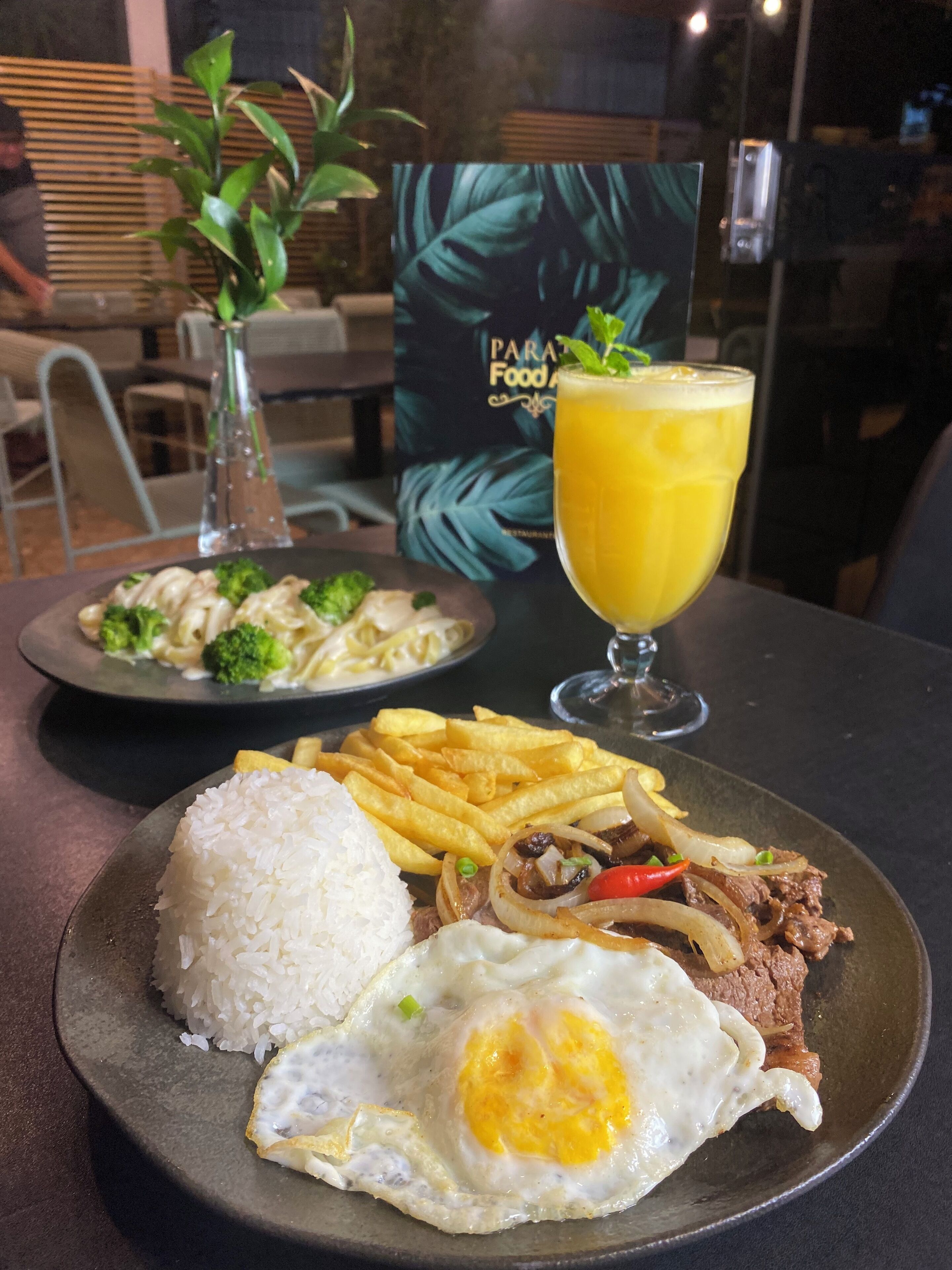 A plate of food with rice, fried egg, beef, and fries, and a glass of orange juice on a table.