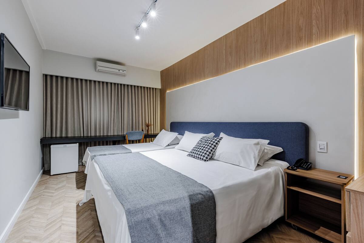 A hotel room with two beds, a desk, a chair, and a TV.