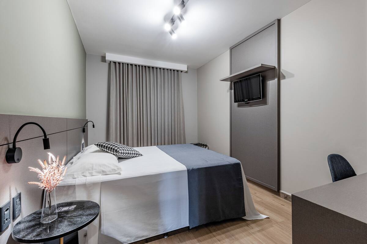 A modern hotel room with a bed, bedside table, and a TV mounted on the wall.
