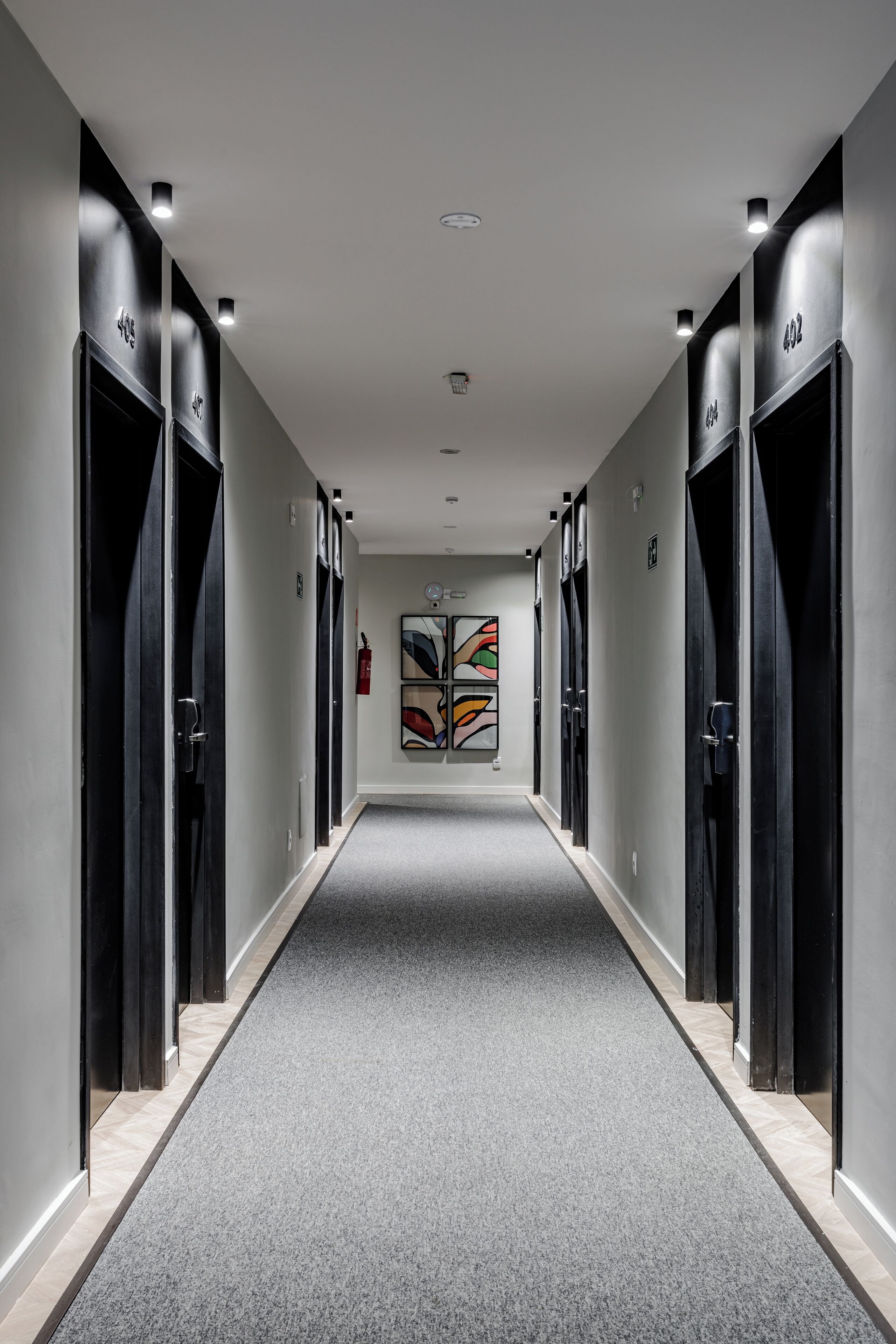 A modern hallway with black elevator doors, a grey carpet, and a colorful abstract painting on the wall.