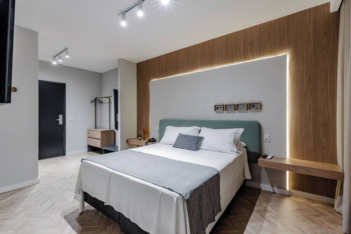 A modern bedroom with a large bed, bedside tables, a nightstand, a mirror, and a wooden accent wall.
