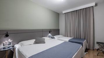 Habitación de hotel con dos camas, una mesita de noche con lámpara, luz en la pared y ventana con cortinas.