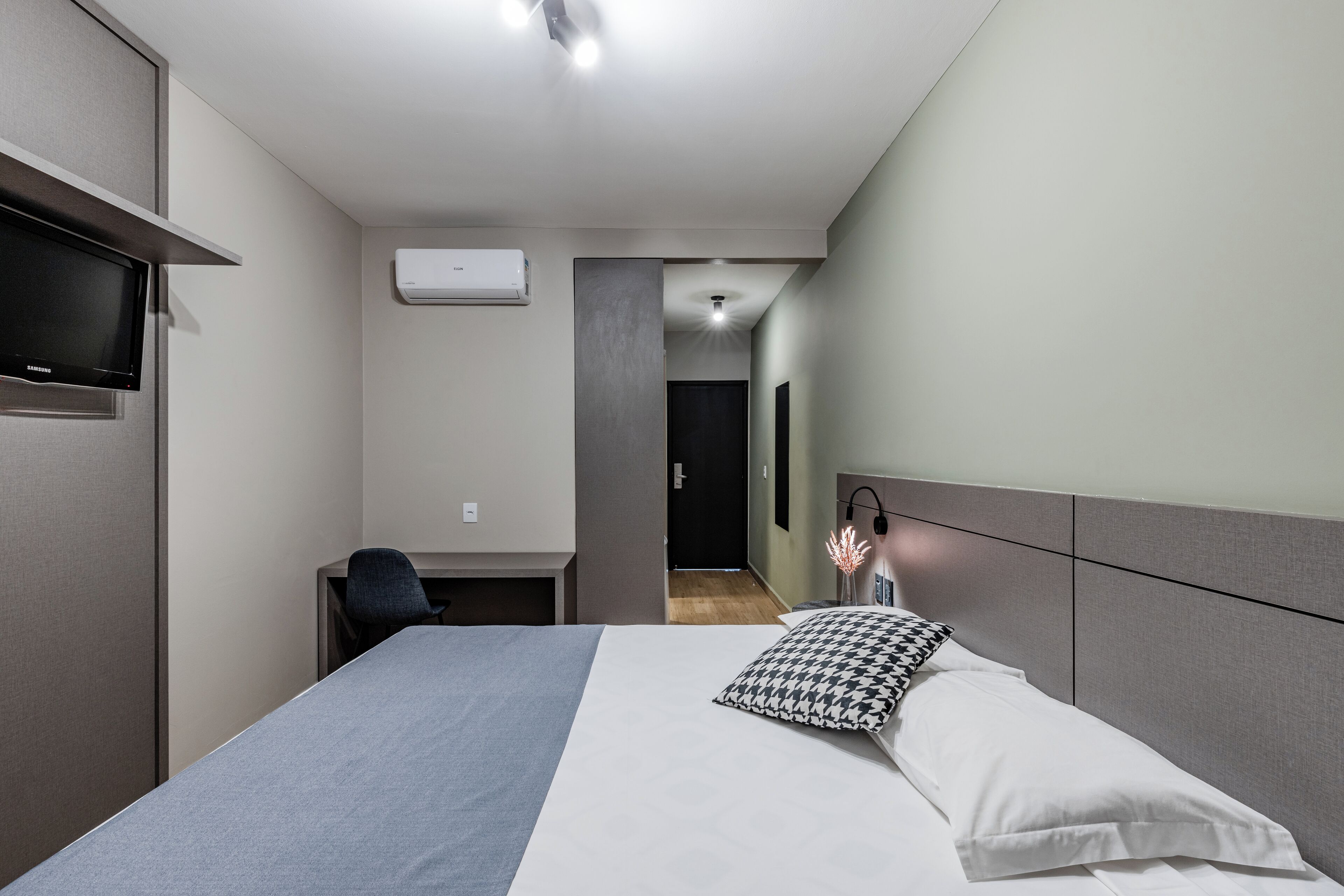 Une chambre d’hôtel moderne équipée d’un lit, d’un bureau, d’une chaise, d’une télévision et d’un appareil de climatisation.