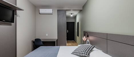 Une chambre d’hôtel moderne équipée d’un lit, d’un bureau, d’une chaise, d’une télévision et d’un appareil de climatisation.