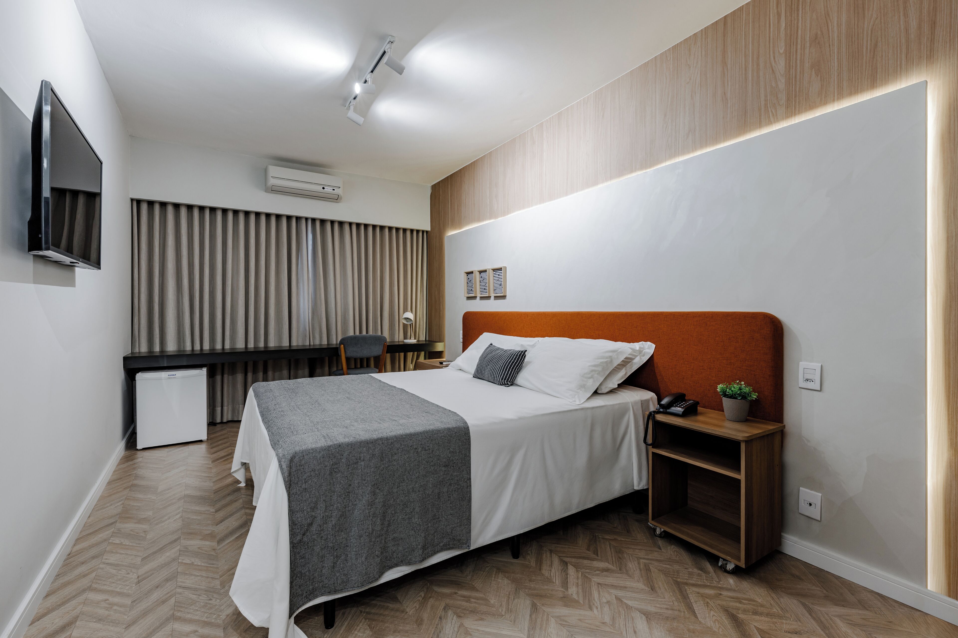 A modern hotel room with a large bed, a desk, and a television.